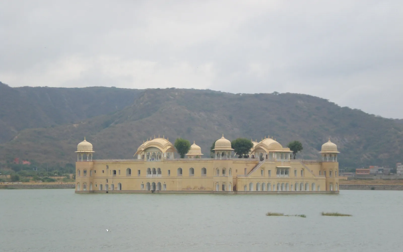 Der Wasserpalast in Jaipur, ein heller Palast mitten in einem See vor Bergen